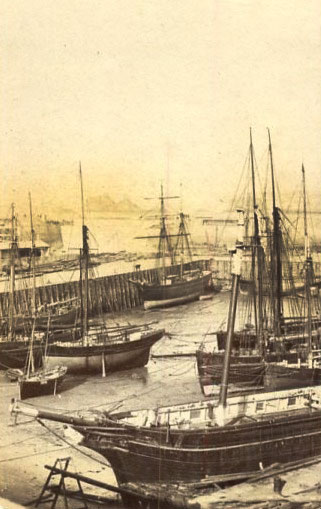 After careful study of the two images we are confident that they are different photographs taken from the same viewpoint within a short time of each other. The only discernable differences are the stance of the figure on the edge of the pier behind the ship in the centre of the picture, and the dog, which appears on the harbour bed close to the centre of the picture on the left, but is missing in the picture above. The image on the left is of much higher quality than this one. This could be down to how the two copies have been stored over the years