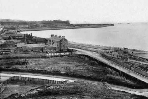View across West Park area to St Helier Harbour and Fort Regent from Westmount in the 1880s. The Marine Hotel and Baths in the middle, later the site of the Grand Hotel, with derelict site covered in rubble and timber alongside, part of West Park station in construction, and the bare site of Traingle Park