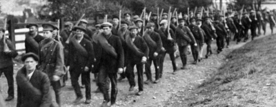 South Staffordshire Regiment in Jersey: recruits on a route march passing through an unidentified location. Most have no uniforms, some have been issued rifles by this time and all have a blanket roll over their shoulders, suggesting they may be sleeping outside that evening.
