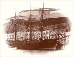 A large sailing vessel moored alongside Commercial Buildings with Fort Regent in the background